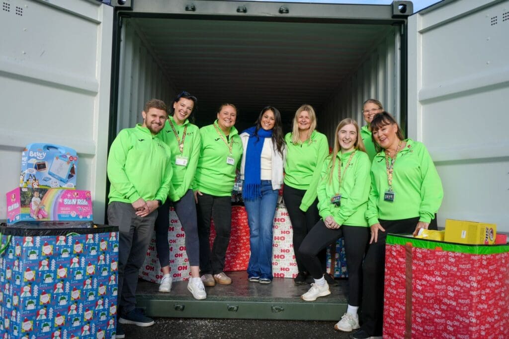 Eight volunteers pose inside a storage container surrounded by wrapped Christmas gifts