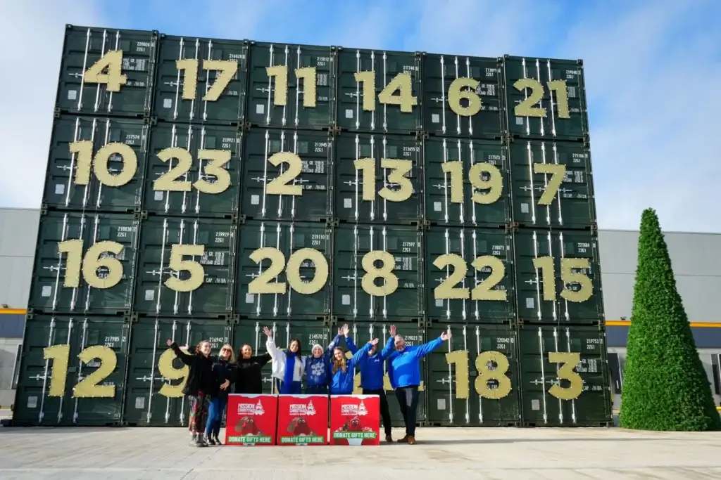 Cuboid team members stand beside numbered storage containers and red Christmas donation boxes