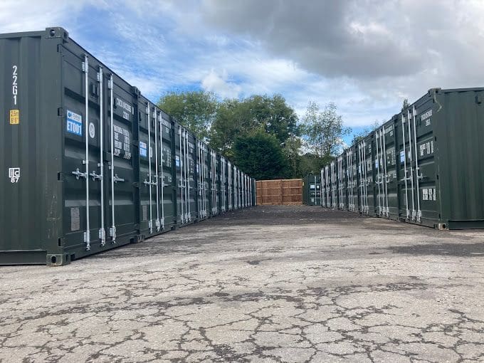 Rows of dark storage containers line both sides of a paved self-storage facility yard