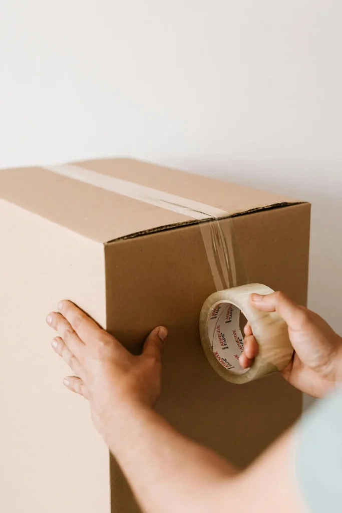 Hands sealing a cardboard moving box with clear packing tape